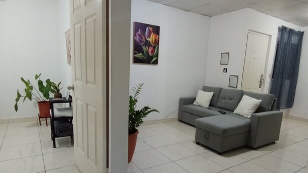 A spacious living room with a grey sofa, a potted plant, and a tiled floor. - Copeyhousechiriquí (Volcán)