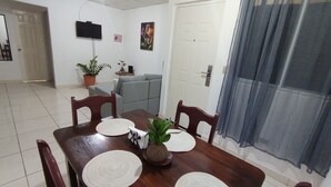 A dining area with a wooden table, four chairs, and two placemats. A potted plant is on the table, and a sofa is in the background. - Copeyhousechiriquí (Volcán)