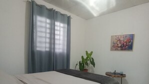 A bedroom with a bed, a potted plant, a painting, and a small table. - Copeyhousechiriquí (Volcán)