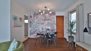 Un espace repas comprenant une table ronde, des chaises noires, un lustre moderne et une grande fresque murale abstraite.