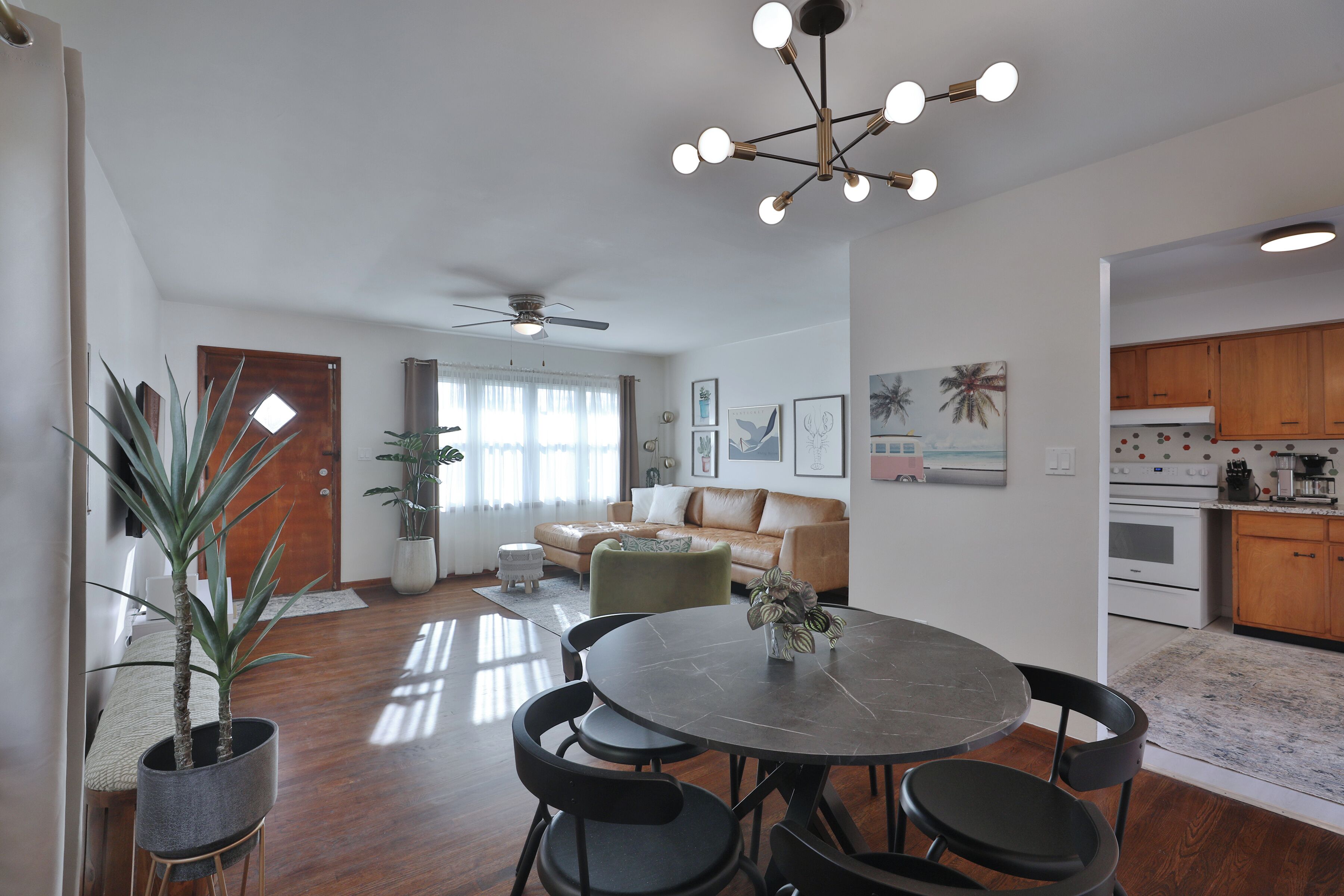 A modern living room with a dining area, a kitchen, and a ceiling fan.