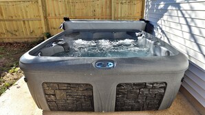 Un bain à remous doté d’un panneau de commande, situé à l’extérieur, près d’une clôture en bois et d’une maison.