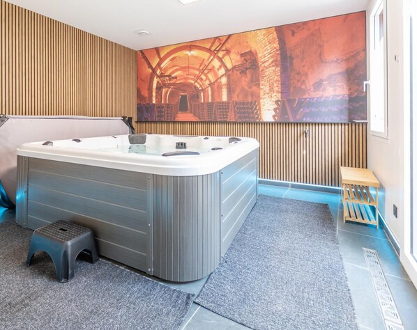 A modern bathroom with a large bathtub, wooden paneling, a small wooden stool, and a large mural on the wall.