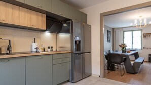 A modern kitchen with grey cabinets, a stainless steel refrigerator, and a dining area with a table and chairs.