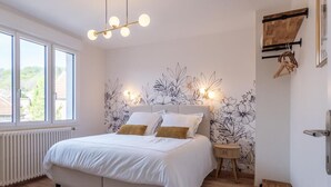 A bedroom with a bed, a nightstand, a wooden bench, and a wall with a floral pattern.