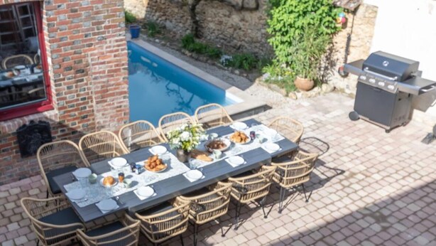 An outdoor dining area with a pool, wicker chairs, and a barbecue grill.