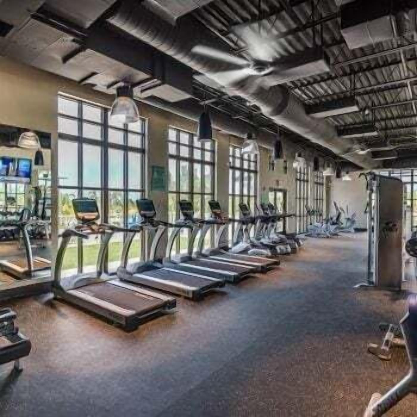 A gym with treadmills, exercise equipment, and large windows.