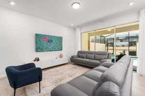 Een moderne woonkamer met een grijze bank, een blauwe fauteuil, een witte salontafel en een grote televisie.