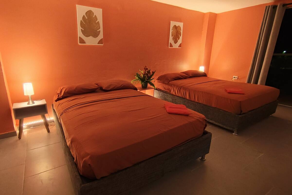A hotel room with two beds, a nightstand with a lamp, and a potted plant.