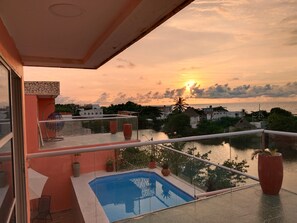 A balcony with a pool, overlooking a sunset over a body of water with buildings in the background. - Hotel Casa Harmony (Cartagena)