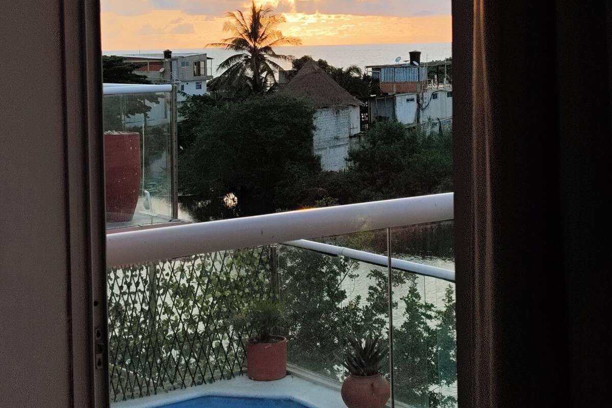 A balcony with a view of a sunset over a body of water, potted plants, and a pool.