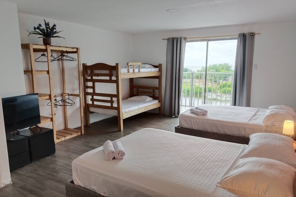 A hotel room with two beds, a TV, a wooden shelf with clothes, and a window with a view.