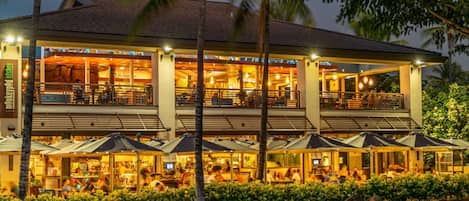 A multi-story hotel with outdoor seating and palm trees.