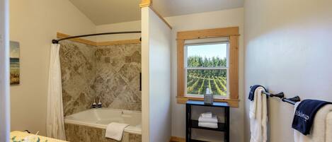A bathroom with a shower, bathtub, and a window with a view of a vineyard.