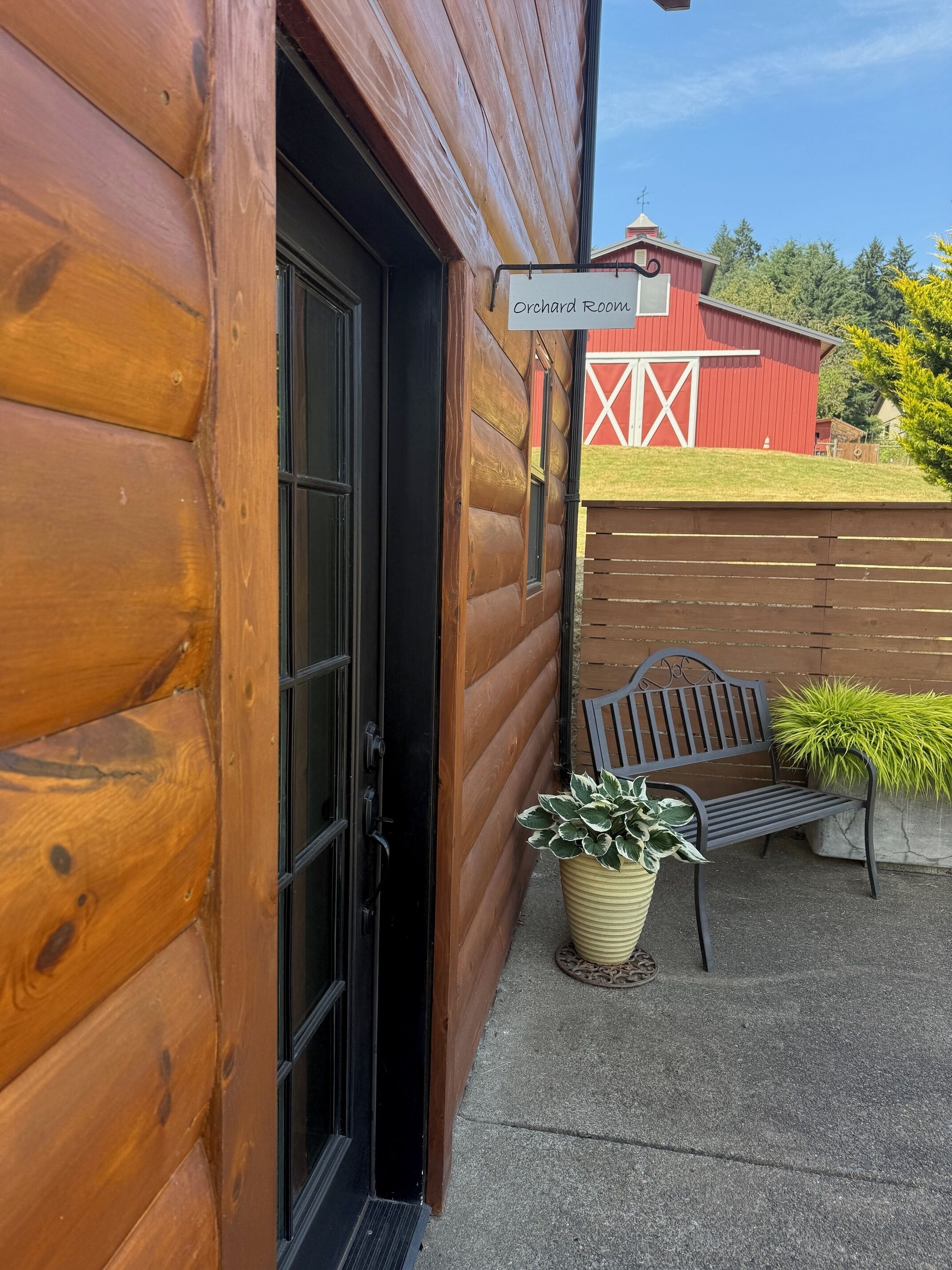 A wooden log building with a sign reading 'Orchard Room,' a bench, and a potted plant.