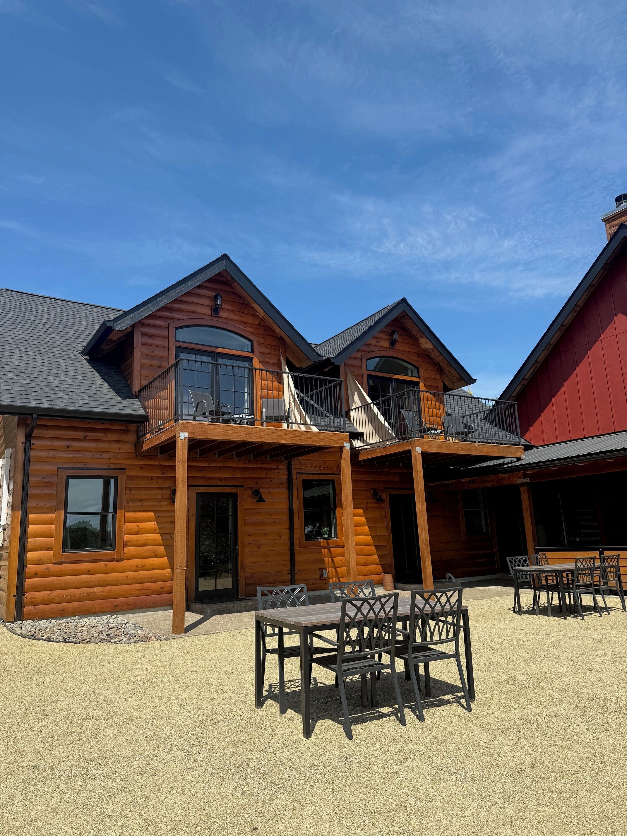 A log cabin with a balcony, a covered patio, and outdoor seating.