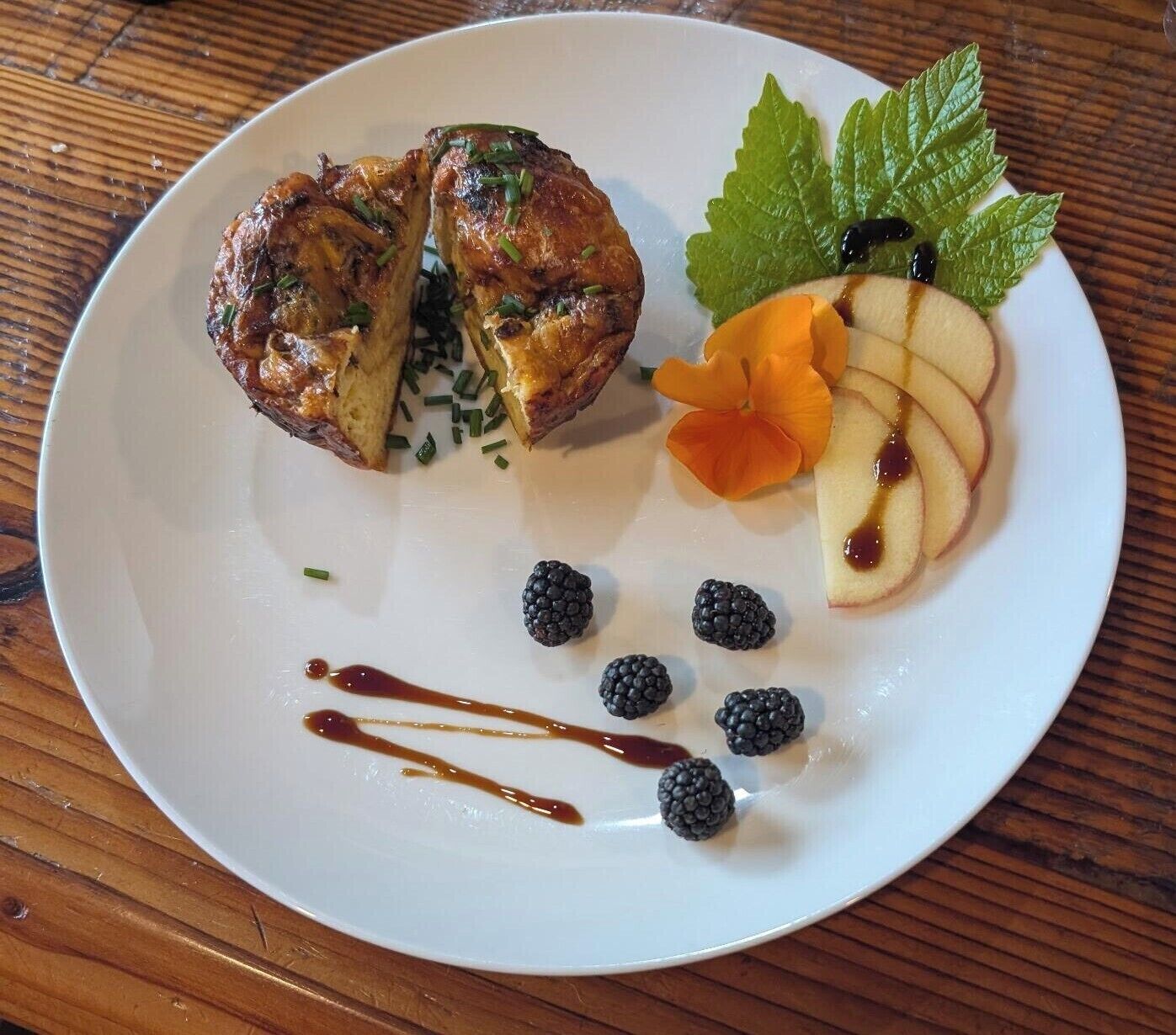 A plate with a meat dish, apple slices, blackberries, and a mint leaf.