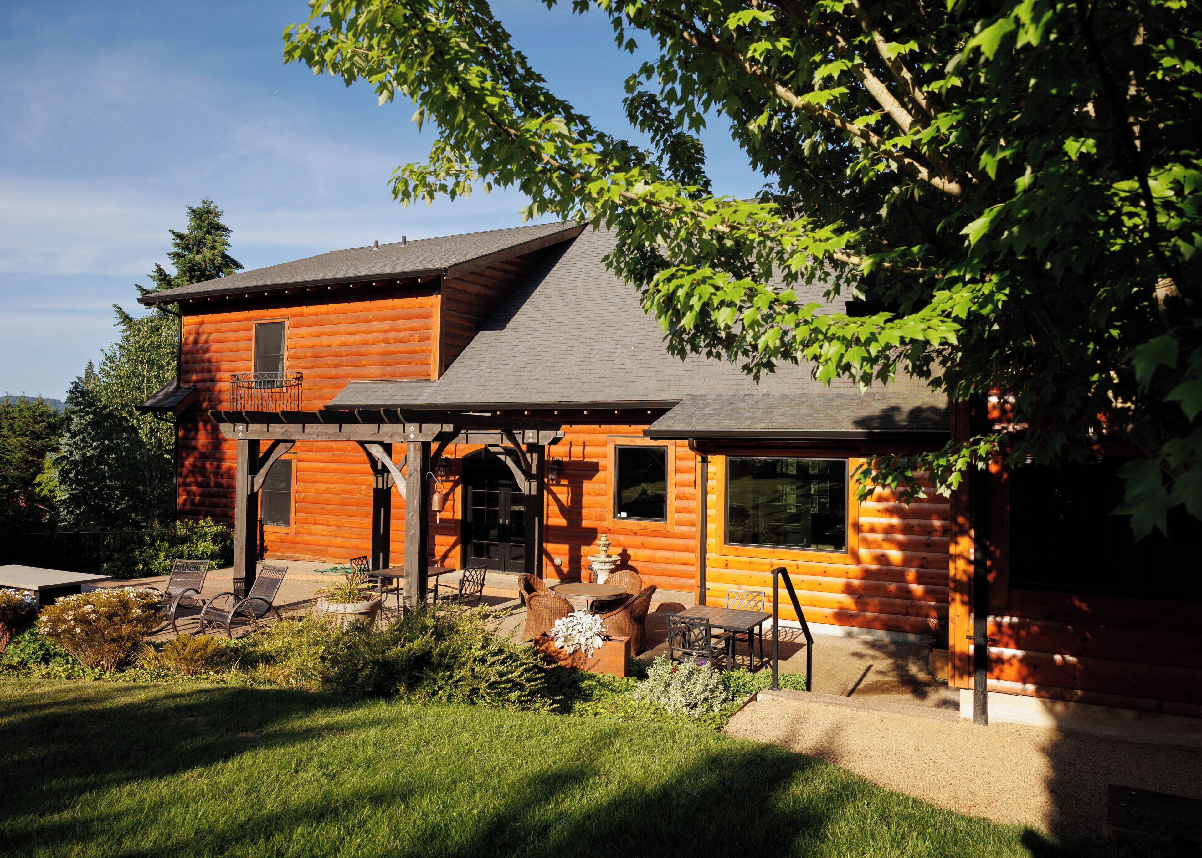 A log cabin with a balcony, a patio with outdoor seating, and a view of the surrounding landscape.