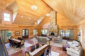 Un intérieur spacieux de chalet en bois avec une cheminée en pierre, un coin repas et de nombreux espaces pour s’asseoir.