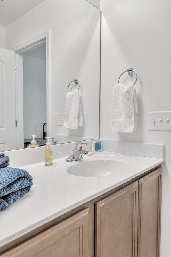 Un baño moderno con un lavamanos blanco, dos anillas para toallas y un espejo que refleja la habitación.