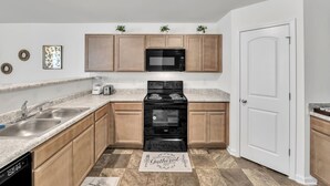 Una cocina con armarios de madera, un microondas negro, una estufa y un lavavajillas.