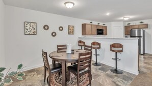 Una cocina moderna con armarios de madera, una isla central con taburetes y una zona de comedor con una mesa redonda y sillas.
