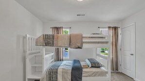 Habitación con literas, paredes blancas, una ventana con cortinas y una puerta.