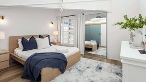 A modern bedroom with a wooden bed, bedside lamps, a large mirror, and a potted plant. - Woolstore Style! ~ 2Bed/2Bath/1Car ~ Teneriffe (Teneriffe)