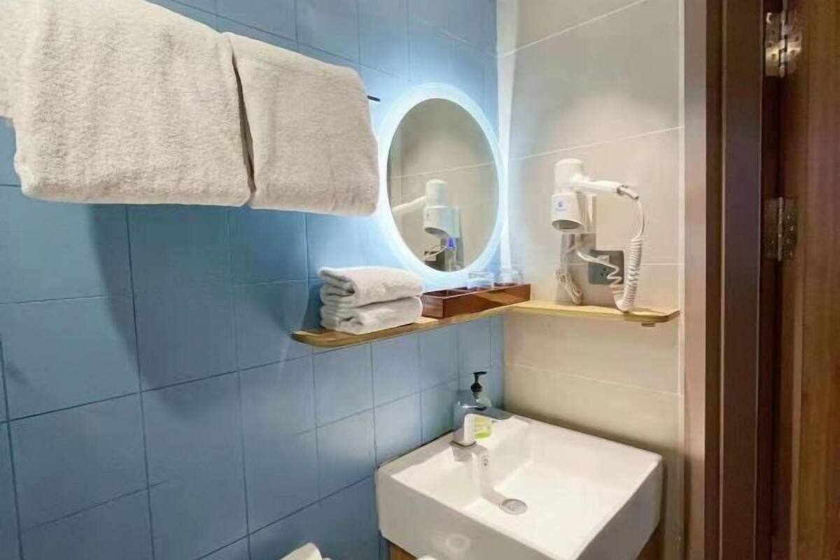 Ein Badezimmer mit blauen Fliesen, einem weißen Waschbecken, einem Spiegel mit Beleuchtung und einem Handtuchhalter.