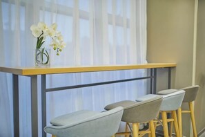 A dining area with a table and chairs, a vase with flowers, and a window with sheer curtains.