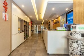 A hotel reception area with a reception desk, shelves with books, and a wall with a red decoration. - Shanghai Yaya Light Luxury Hotel (Hongkou Football Stadium) (Shanghai)