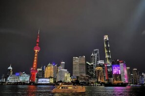 A city skyline at night with illuminated buildings and a boat in the foreground.