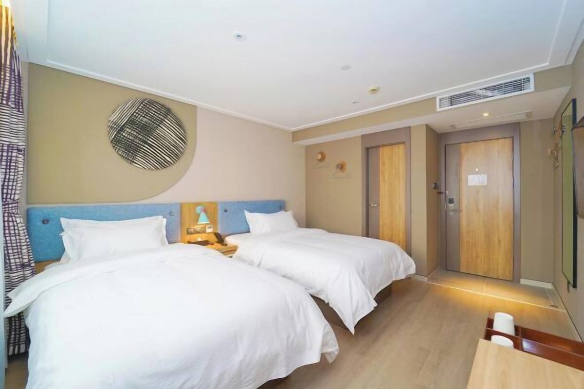 Ein Hotelzimmer mit zwei Betten, einem Nachttisch mit Lampe, einer Wanduhr und einer Tür.