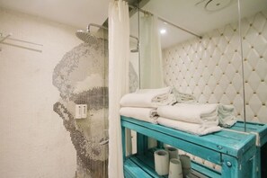 Une salle de bain avec une douche, un porte-serviettes et une étagère contenant des serviettes et du papier toilette.