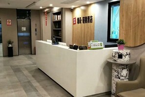 A hotel reception area with a reception desk, a small table with a plant, and a wall-mounted television.