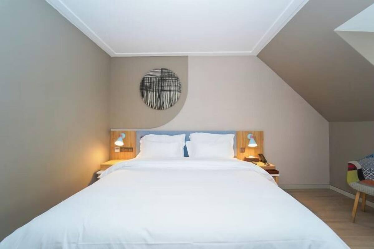 Ein Schlafzimmer mit einem Bett, zwei Nachttischen, einem Wandbild und einem Sessel.