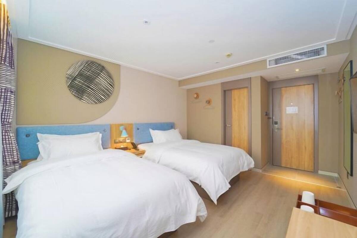 Ein Hotelzimmer mit zwei Betten, einem Nachttisch mit Lampe, einer Wanduhr und einer Tür.