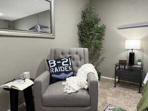 A room with a grey armchair, a small table with a mug and glasses, a lamp, a plant, and a wall-mounted mirror. - Abilene Icon- Sky, Story, and the Western Spirit! (Abilene)