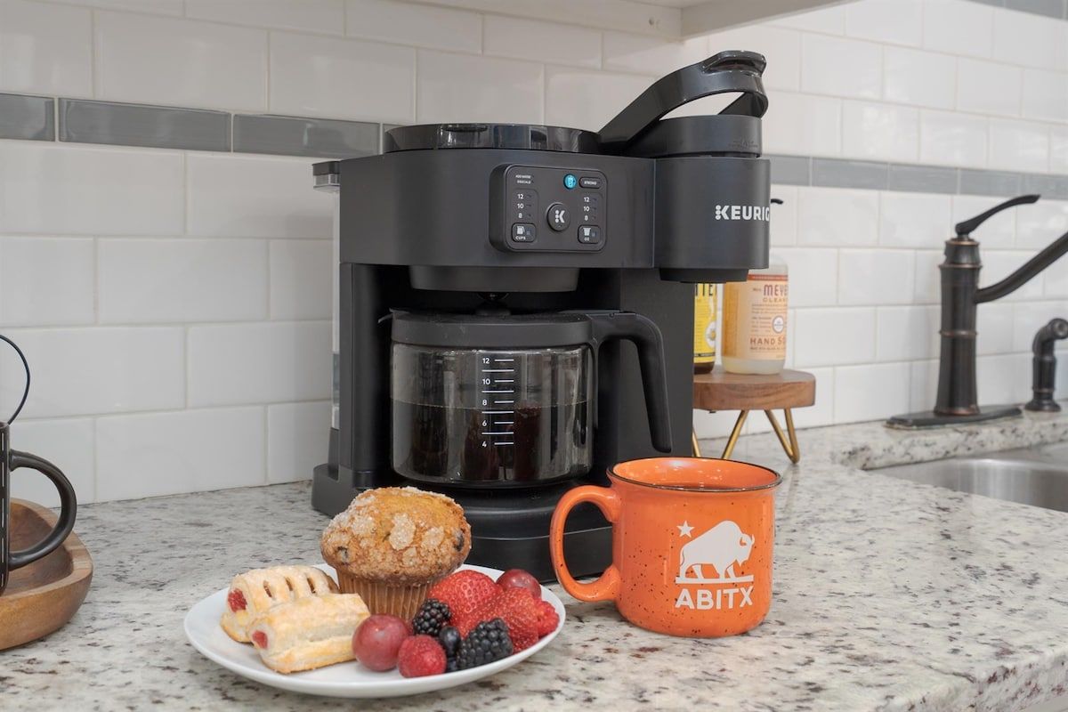 Eine Küche mit einer Keurig-Kaffeemaschine, einer Platte Gebäck und Beeren sowie einer orangefarbenen Tasse mit einem Büffel-Logo.