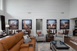 A spacious living room with a brown sofa, armchairs, and a coffee table. There are framed pictures on the walls and a door leading to another room. - Abilene Icon- Sky, Story, and the Western Spirit! (Abilene)