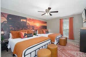 A bedroom with two beds, a ceiling fan, a large wall mural, a window with curtains, and a dresser. - Abilene Icon- Sky, Story, and the Western Spirit! (Abilene)
