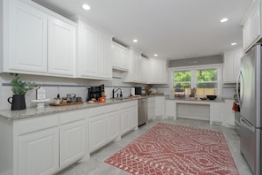 Una cocina moderna con armarios blancos, encimeras de granito, electrodomésticos de acero inoxidable y una alfombra roja con estampado.
