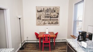 Cocina compacta con una mesa de comedor, sillas rojas, cafetera y una obra de arte colgada en la pared.