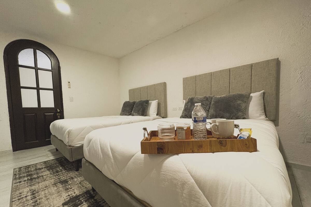 Habitación de hotel con dos camas, una bandeja de madera con artículos de aseo y una puerta con paneles de vidrio esmerilado.