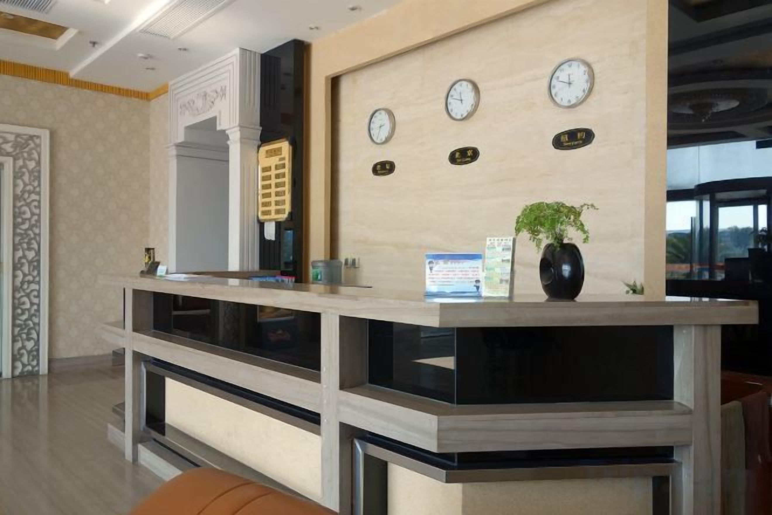 Un comptoir d’accueil avec une horloge, un vase avec une plante et un tableau encadré au mur.