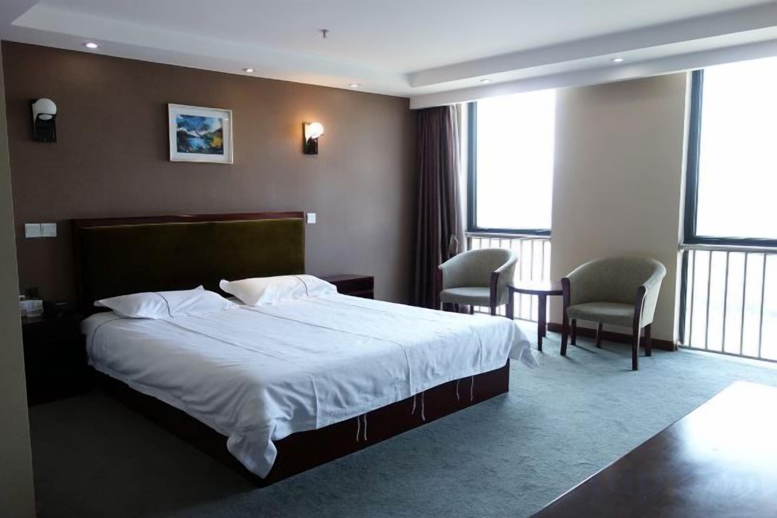 A hotel room with a large bed, a chair, a small table, and a view of the outdoors.