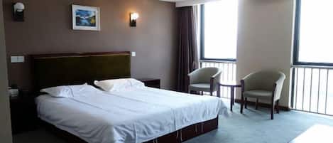 A hotel room with a large bed, a chair, a small table, and a view of the outdoors.