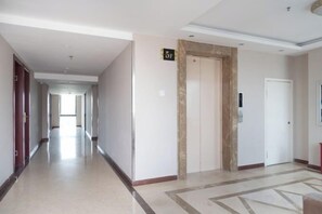 Un couloir d’hôtel avec un ascenseur fermé, une porte avec une pancarte et un tapis à motifs.