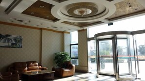A lobby with a brown leather sofa, a coffee table, a potted plant, and a revolving door. - Yongxiang Business Hotel (Shanghai)
