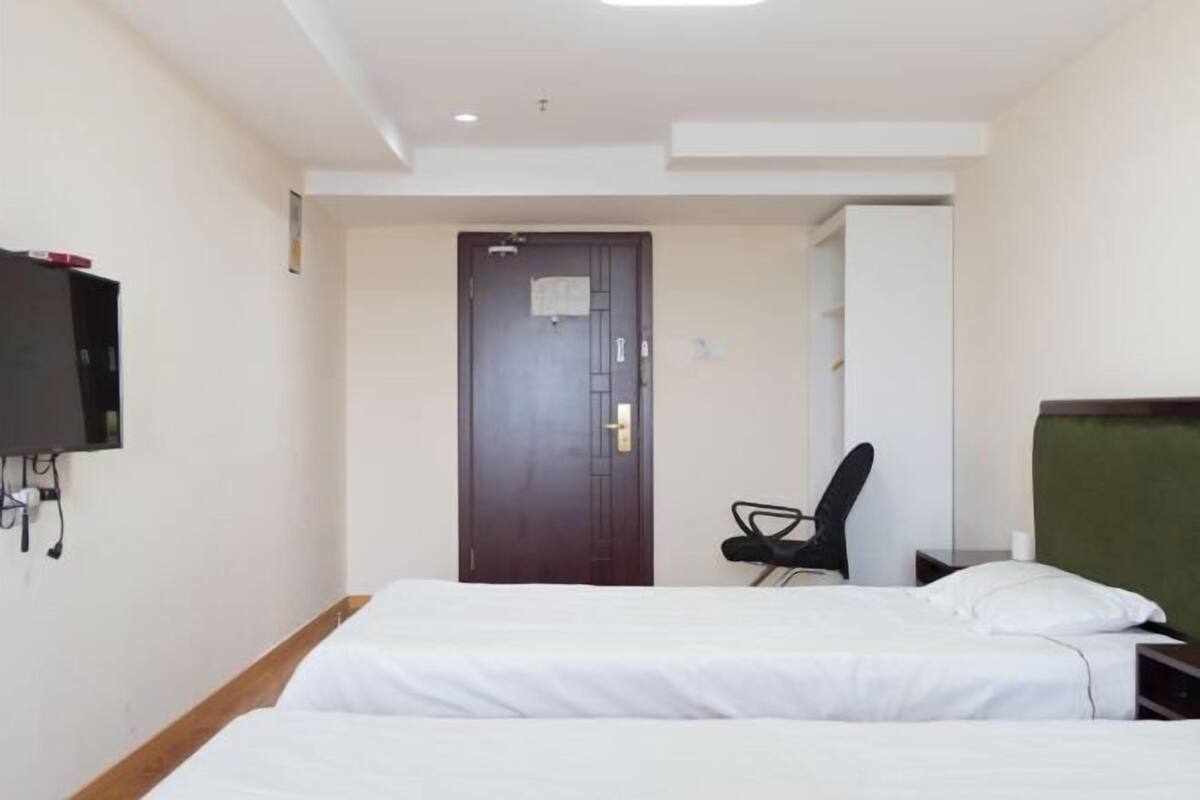 Una habitació d'hotel amb dos llits, un escriptori, una cadira i una televisió penjada a la paret.